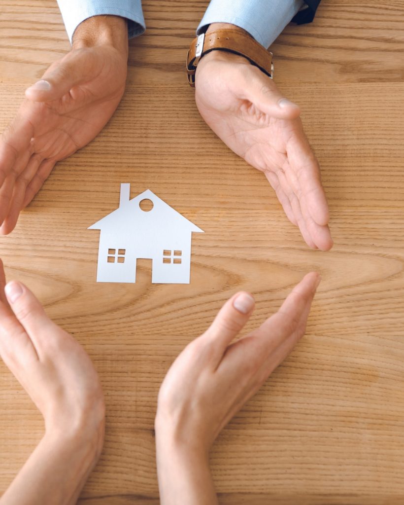 partial view of insurance agents and female hands with paper house model on wooden tabletop, house